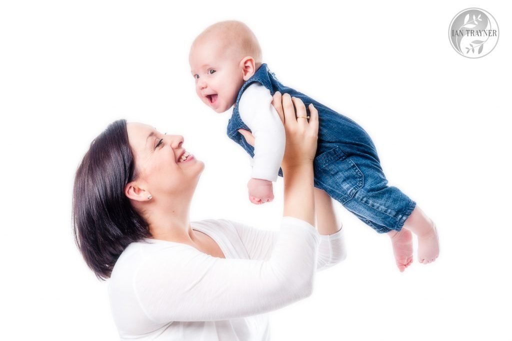 High key photo of mother and baby. She is holding him up high. Very happy photo.